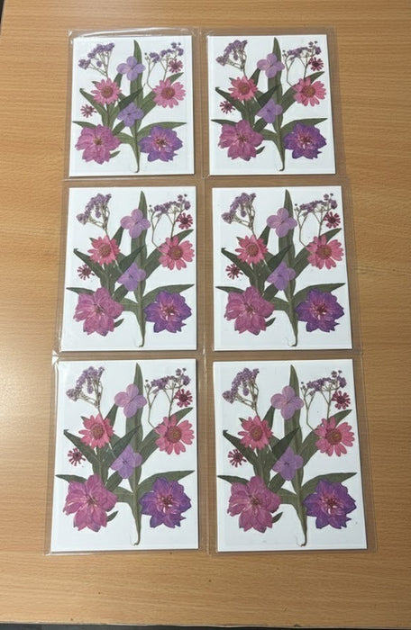 Handcrafted botanical art print featuring real purple and pink pressed flowers on a white wood background. The print is styled as a greeting card and also shown framed, ready for home decor.