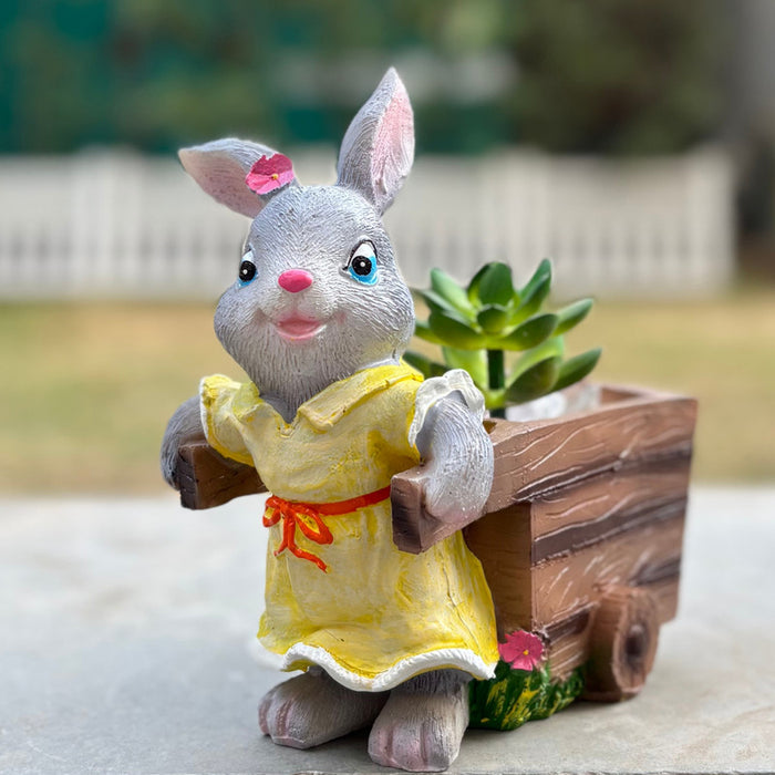 Close-up of a decorative grey bunny succulent planter wearing a yellow dress and pulling a brown wooden cart