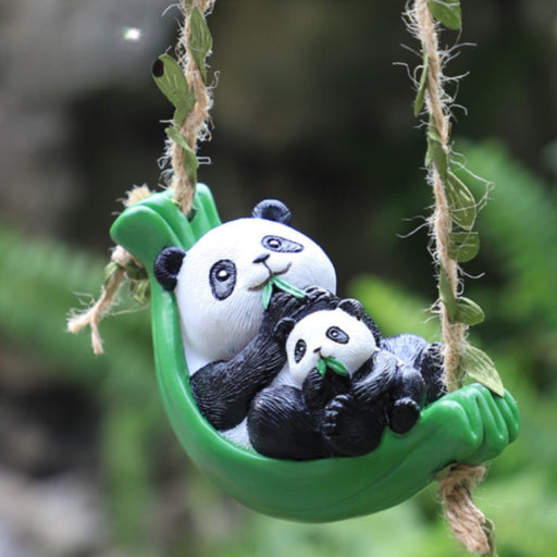 A hanging garden ornament featuring a mother and baby panda sitting in a green bamboo leaf swing, suspended by rustic ropes with faux leaves against a blurred green background.