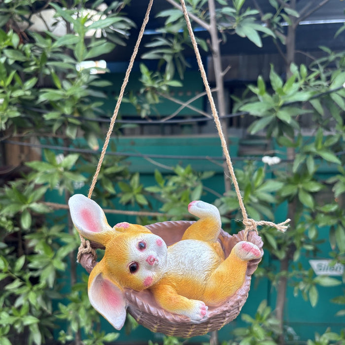 Cute yellow rabbit figurine sitting in a hanging basket swing