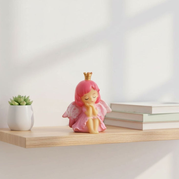 Pink angel princess cake topper with gold crown, delicate wings, and hands clasped in a peaceful pose, mini resin fairy figurine isolated on a white background.