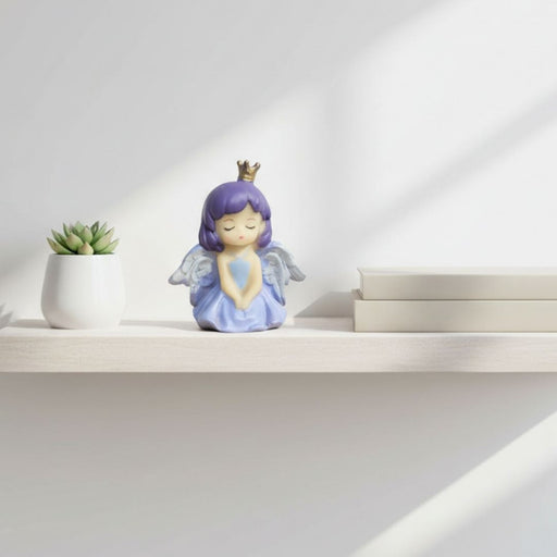 Close-up of a small, resin angel princess cake topper with eyes closed, purple hair, a gold crown, and light blue/lavender wings and dress.