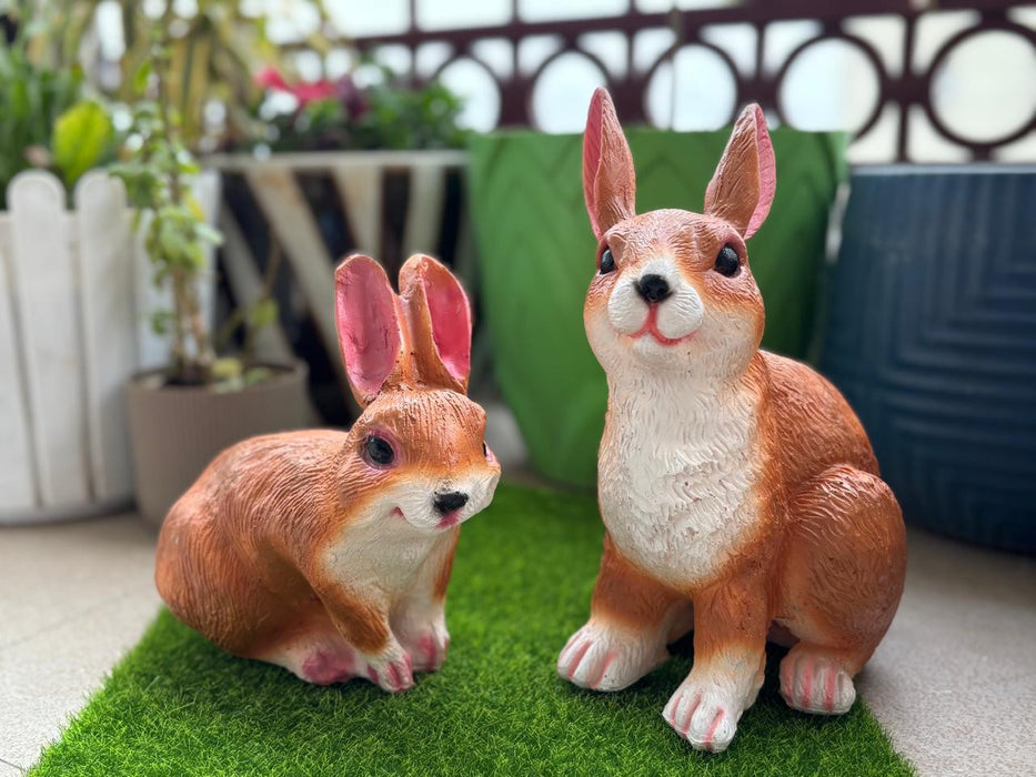 Two Dark brown ceramic rabbit figurines with pink ears and red eyes sitting on a grey floor.