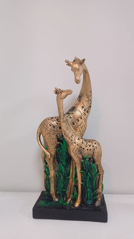 Two golden giraffe statues standing among green foliage, featuring intricate black and gold tribal patterns. The statue is mounted on a black base.
