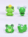 Four small, green, whimsical frog figurines. One wears a yellow crown, one has a black bow tie, one has a heart on its chest, and one is smiling while lying down.
