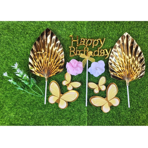 Packaged gold Happy Birthday acrylic cake topper set with pleated fan, pink and white artificial flowers, and gold floral accents.