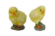 Two adorable yellow chick figurines, one standing on a mossy rock and the other slightly looking down, both with bright orange beaks and feet, isolated on a white background.