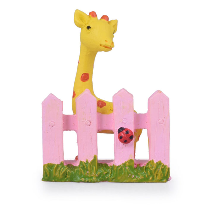 Miniature yellow giraffe figurine behind a pink picket fence with a ladybug detail, decorative resin animal for fairy gardens and terrariums.