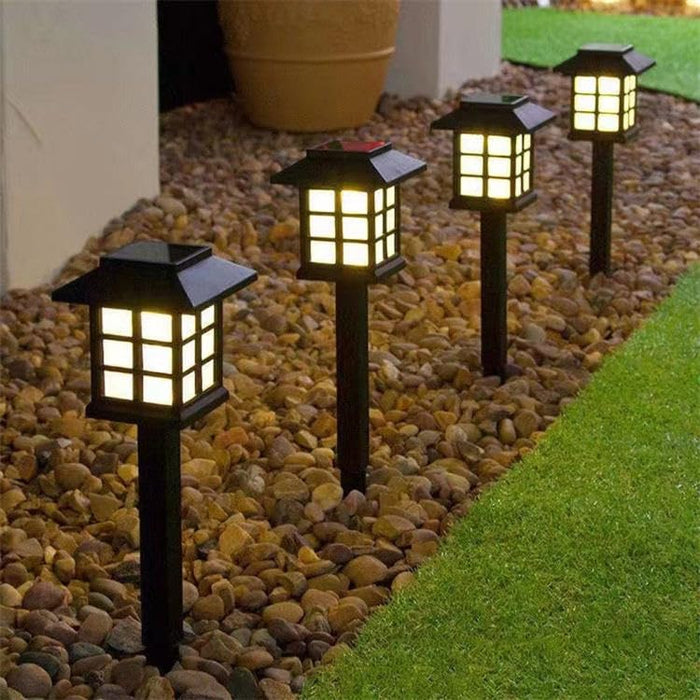 Four black solar pathway lights with a warm white glow, designed in a classic Japanese lantern style, installed along a rock garden border next to a lawn.