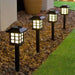 Four black solar pathway lights with a warm white glow, designed in a classic Japanese lantern style, installed along a rock garden border next to a lawn.