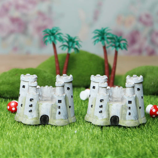 Two miniature grey resin medieval castle figurines with multiple towers and subtle green mossy bases, shown side-by-side against a solid white background.