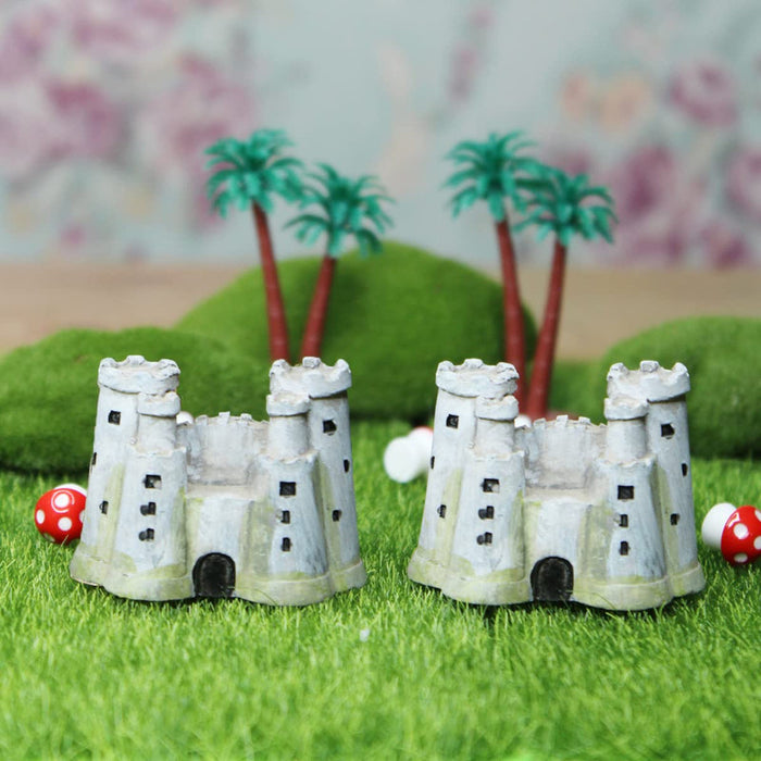 Two miniature grey resin medieval castle figurines with multiple towers and subtle green mossy bases, shown side-by-side against a solid white background.