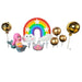 Close-up of a whimsical cake topper set featuring a pink-haired mermaid figurine, a large bright rainbow with white clouds, an iridescent crown pick, and three shiny gold sphere balloon toppers on sticks, all on a wooden surface.