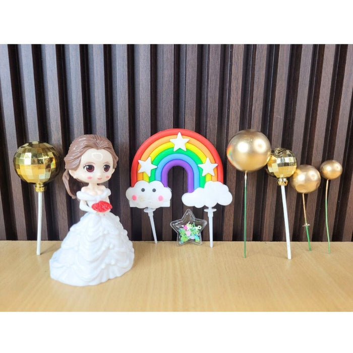 Little Princess doll cake topper set in clear packaging, including a doll in a white dress, three gold spherical balloon toppers, a colorful rainbow decoration, and a 'PARTY' banner. Perfect for a girls' birthday or baby shower cake.