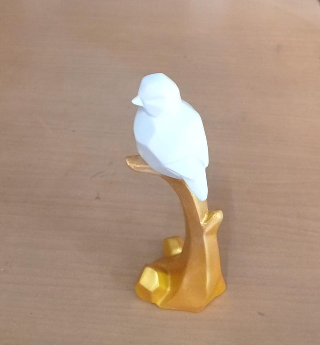 White geometric  bird sculpture perched on a golden branch-like stand against a wood background.