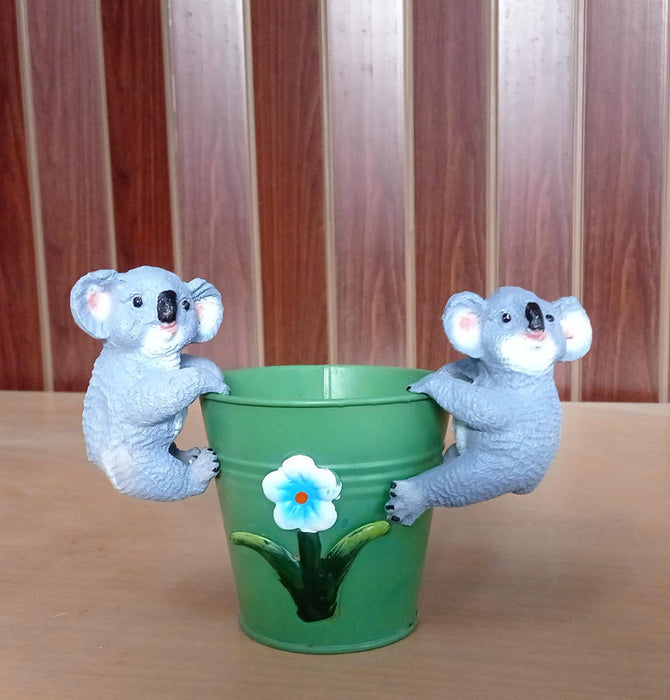 Two cute grey koala figurines clinging to the sides of a planter.