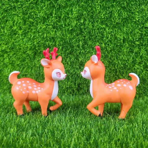 A pair of cute, identical miniature cartoon deer figurines with bright orange coats, white underbellies, rosy cheeks, and reddish-brown antlers standing side-by-side against a solid white background.