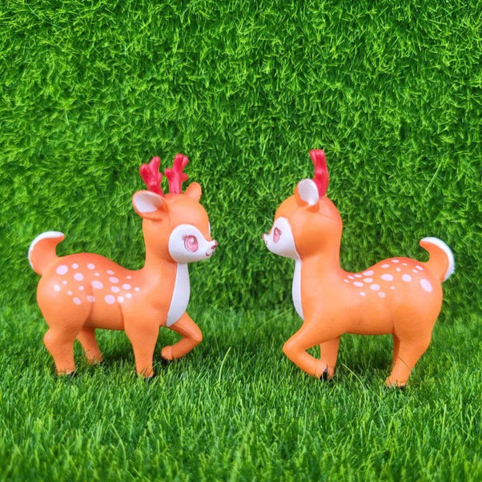 A pair of cute, identical miniature cartoon deer figurines with bright orange coats, white underbellies, rosy cheeks, and reddish-brown antlers standing side-by-side against a solid white background.