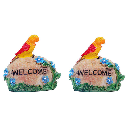 Two identical resin garden ornaments featuring a bright yellow and red parrot perched on a light brown stone that says "WELCOME" in black letters. The stones are decorated with small blue flowers and green leaves.