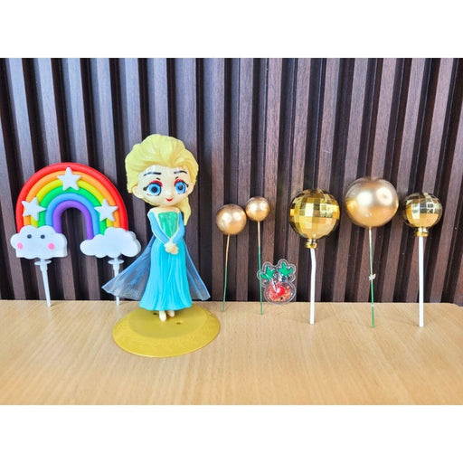 Cake topper set featuring a Princess Elsa doll figure, a rainbow arch, and several gold metallic sphere ornaments for a Frozen-themed birthday party.