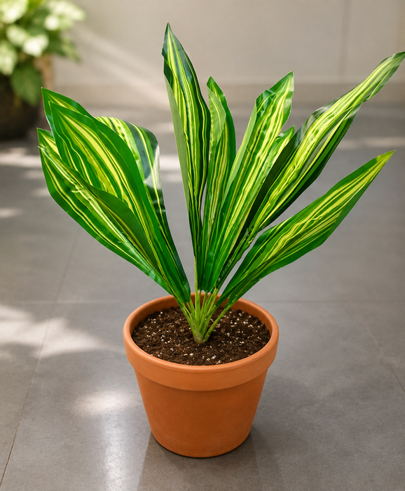 Artificial green dracaena leaf branch held by hand against a grey background.