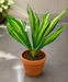 Artificial green dracaena leaf branch held by hand against a grey background.
