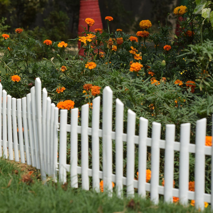 White decorative picket garden edging fence in front of orange marigold flowers and green plants.