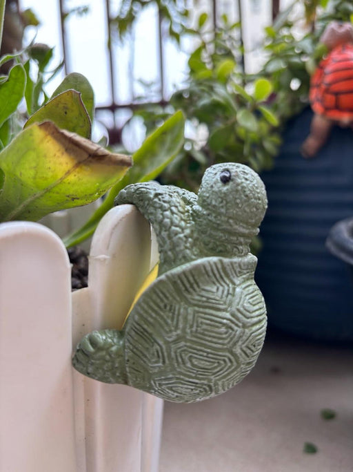 Green moss-textured turtle pot hugger figurine designed to hang on the edge of a flower pot or planter.