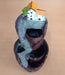 A small, tiered decorative water fountain/cascading incense burner made of resin, featuring two miniature houses with orange roofs perched atop a rocky, cliff-like structure, with the water/smoke path flowing down two bowl-shaped tiers below.