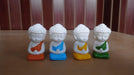 Four small, white, miniature Buddha statues sitting in meditation pose, each with a brightly colored robe in orange, blue, yellow, and green."
