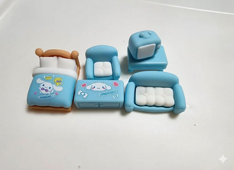 Miniature blue bedroom and living room furniture set, including a bed, sofa, armchair, coffee table, and TV console, with tiny accessory bottles and a cat figure.