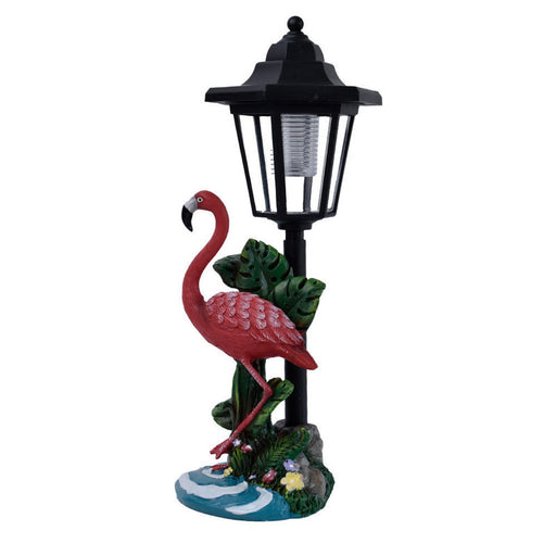Pink flamingo garden statue standing next to a black solar-powered street lantern with yellow LED light on a decorative tropical base.