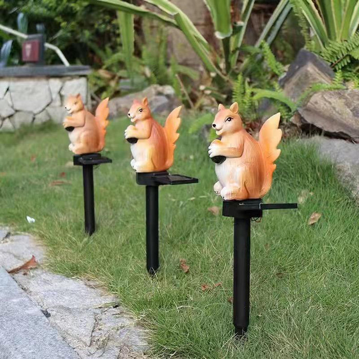 Solar-powered resin squirrel garden stake light glowing with warm orange light in the evening.
