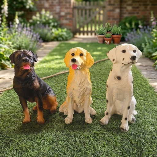 Three realistic hand-painted puppy statues—one black and tan, one golden, and one spotted—sitting together on artificial green grass in an outdoor garden setting.