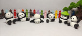 A line of six miniature, cute panda bear figurines in various playful poses, set against a colorful picket fence and a small green bonsai tree.