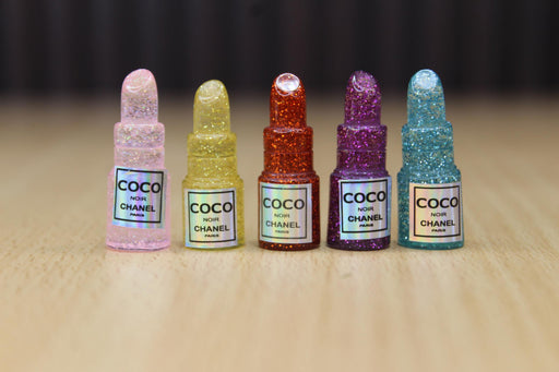 Close-up of five miniature, glitter-filled, lipstick-shaped containers in pink, yellow, orange, purple, and blue