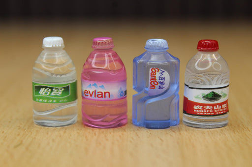 Four miniature replica plastic water bottles lined up on a wooden surface, including detailed models of Nongfu Spring, Evian, Ganten, and another Chinese bottled water brand