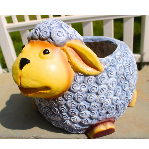 Whimsical sheep planter with a textured blue body and yellow face, sitting on a stone surface outdoors.