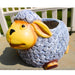 Whimsical sheep planter with a textured blue body and yellow face, sitting on a stone surface outdoors.
