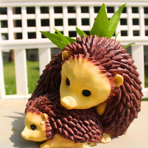 A ceramic planter shaped like two hedgehogs nestled together, one large and one small, with green leaves emerging from the top.