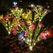 Set of two solar-powered garden stake lights featuring colorful artificial butterflies, pink flowers, and warm white LED fairy lights glowing in a dark backyard garden.