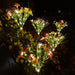 Set of FOUR solar-powered garden stake lights featuring colorful artificial butterflies, pink flowers, and warm white LED fairy lights glowing in a dark backyard garden.