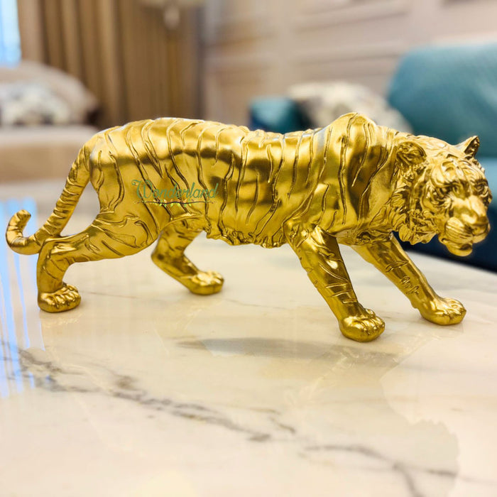Golden tiger figurine with a metallic finish standing on a white marble table in a modern living room.