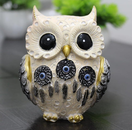 A cream-colored decorative owl figurine featuring ornate scrollwork patterns, gold-tipped ears and talons, and three black dreamcatcher motifs on its chest with blue evil eye (Nazar) centers and dangling feathers.