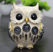 A cream-colored decorative owl figurine featuring ornate scrollwork patterns, gold-tipped ears and talons, and three black dreamcatcher motifs on its chest with blue evil eye (Nazar) centers and dangling feathers.