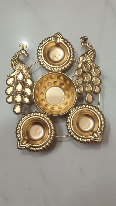 Gold-colored metal peacock diya holder featuring two ornate peacocks, a central hammered bowl, and three traditional diyas. This Panchmukhi-style stand is a perfect auspicious centerpiece for Diwali pooja and festive home decoration.