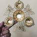 A hand holds a decorative gold-colored metal diya holder designed with four intricate filigree butterflies. The stand features a central bowl surrounded by four traditional oil lamps (diyas), creating a five-wick centerpiece for festive home decor.