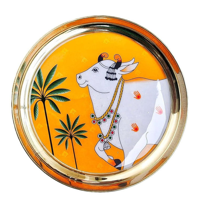 Decorative platter with Pichwai style white cow (Kamadhenu/Nandi) painting on an orange background with palm trees.