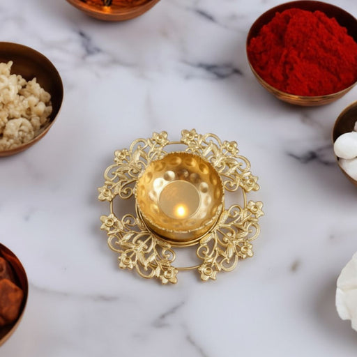Round decorative gold metal Diya holder with intricate floral lattice design. Features a hammered metallic cup holding a burning clay oil lamp (diya) Ideal for tabletop decoration, Diwali, and festive lighting.
