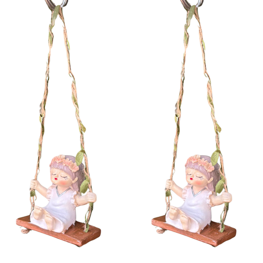 Two identical whimsical resin figurines of a young girl with a flower crown sitting on a wooden-style swing, suspended by twine ropes decorated with green fabric leaves.